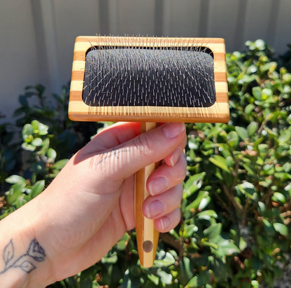 Bamboo Slicker Brush by The Pawfect Trio for pets, showing a wooden handle and metal bristles for grooming pets.